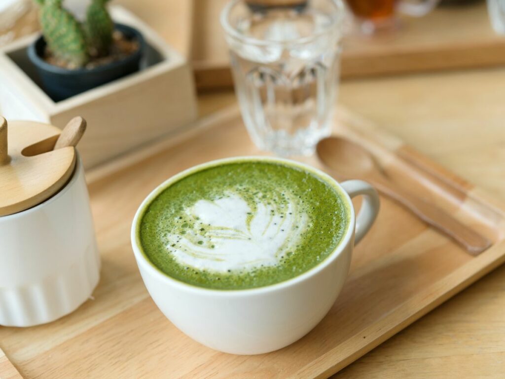 A cup of matcha latte with latte art on top, served on a wooden tray.