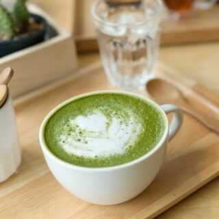 A cup of matcha latte with latte art on top, served on a wooden tray.