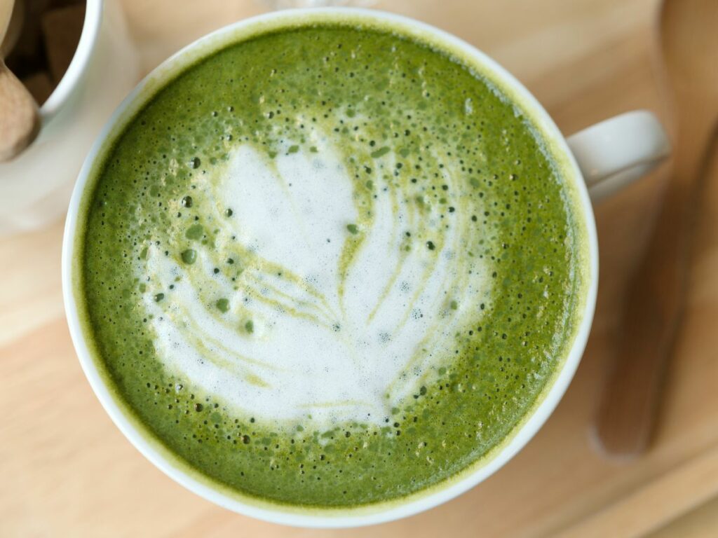 A cup of matcha latte with latte art on a wooden table.