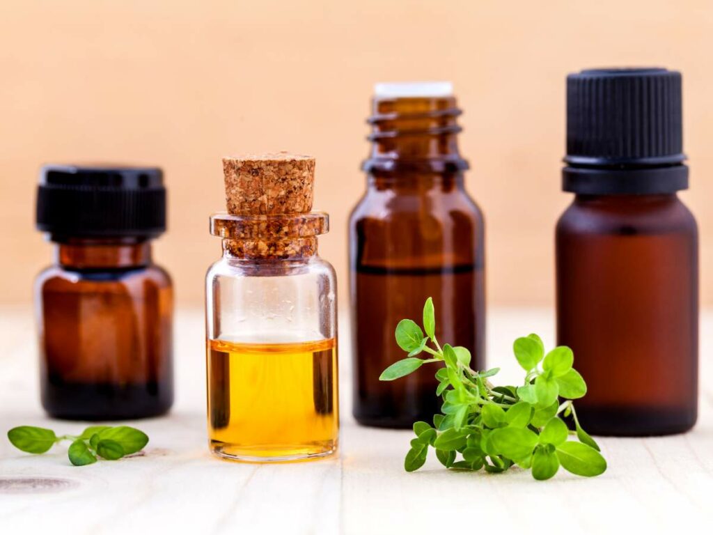 Various sizes of amber glass bottles with essential oils and fresh herbs in the foreground.