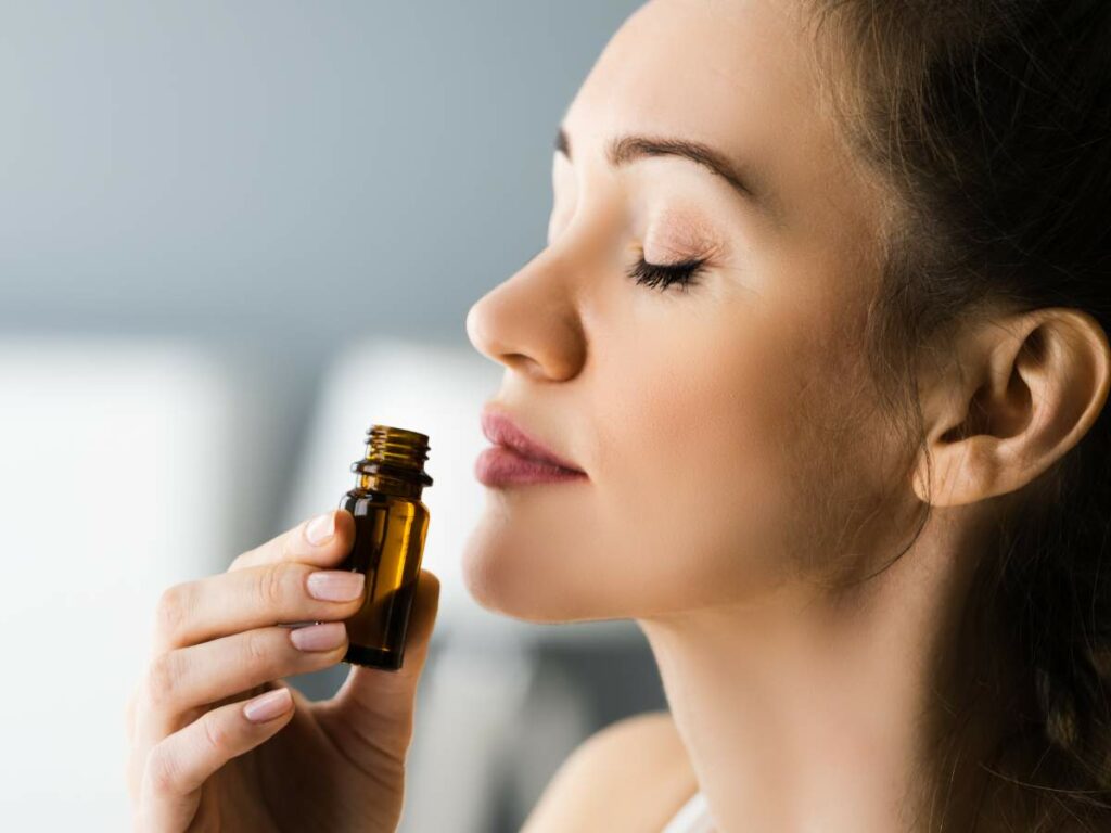 Woman inhaling essential oil from a small amber bottle.