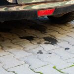 Oil stains on a patterned brick driveway beneath a parked car.
