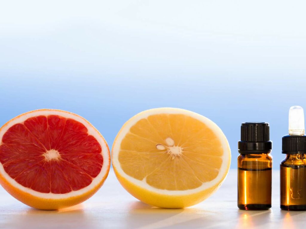 Halved grapefruit and lemon with two small essential oil bottles on a surface, against a blue gradient background.