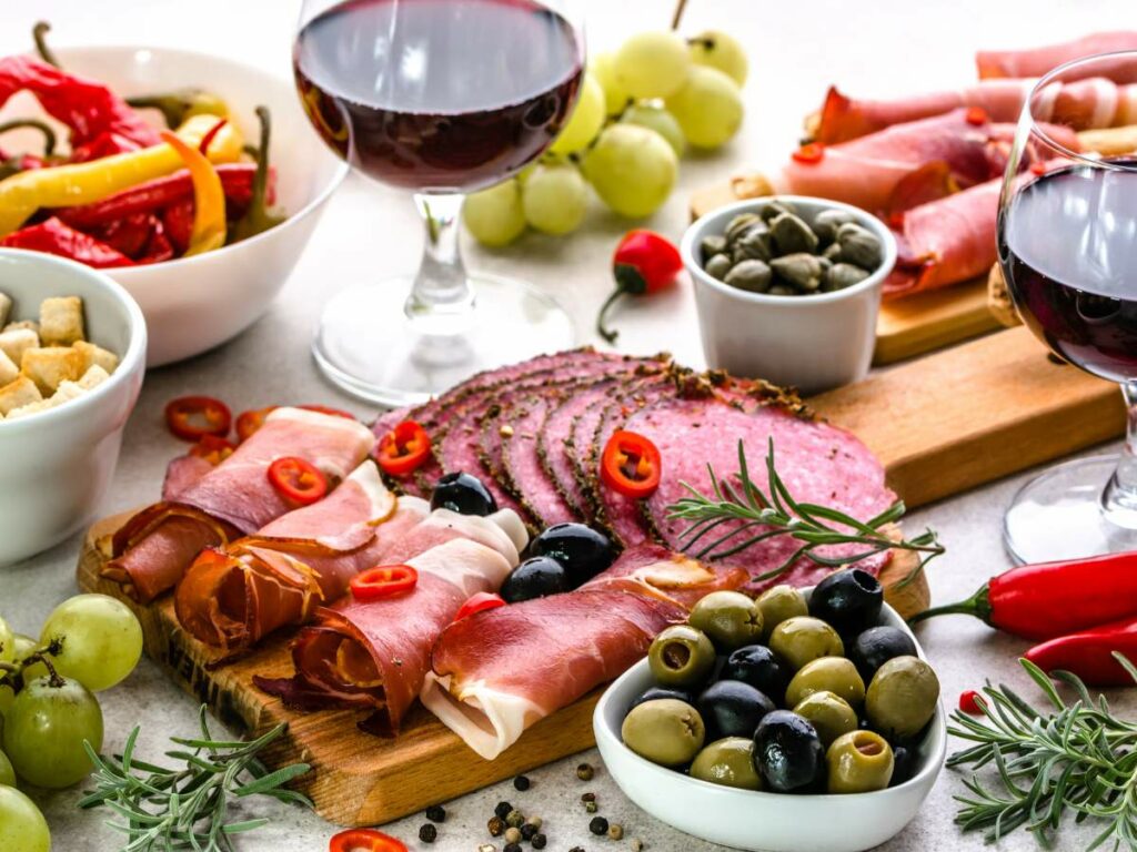 Assorted cured meats, olives, and grapes served with red wine on a table.