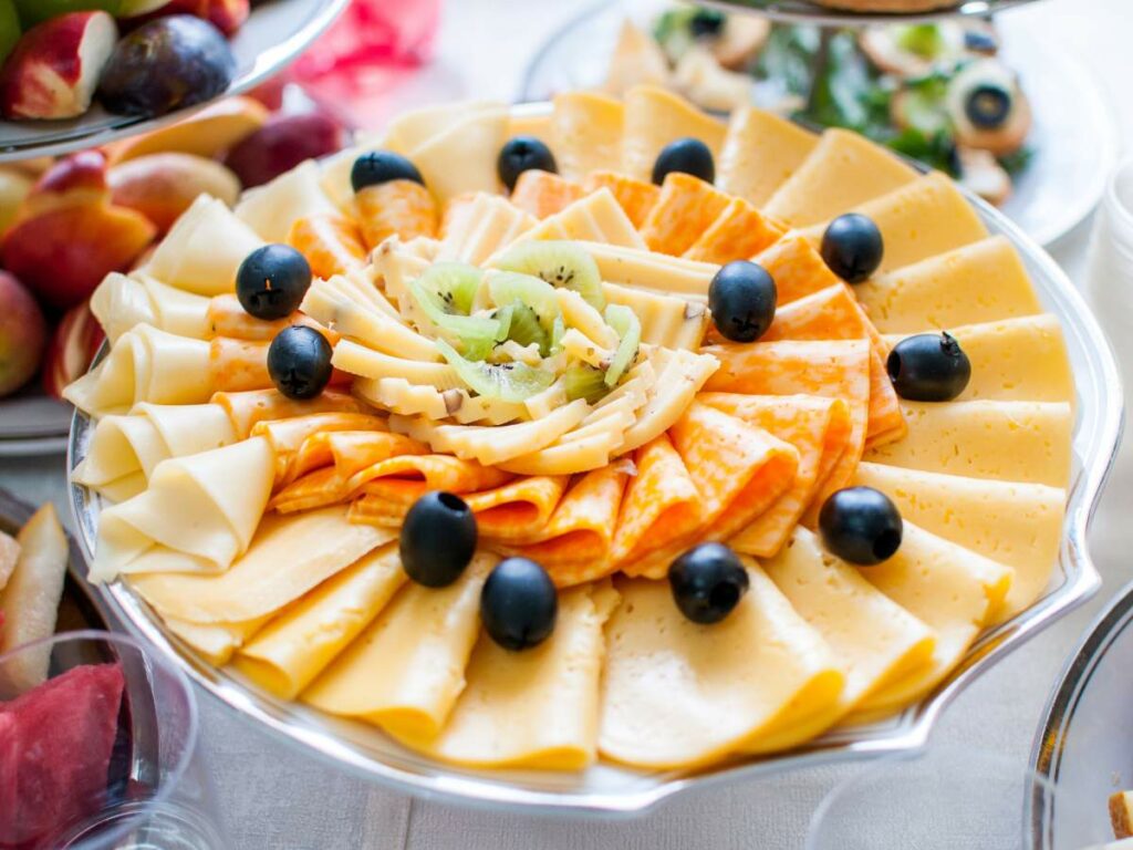 An assortment of sliced cheeses arranged on a wedding platter, garnished with black olives.