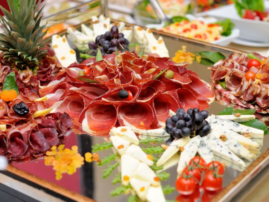 An assortment of cold cuts, cheese, and fruit arranged on a platter for a wedding.