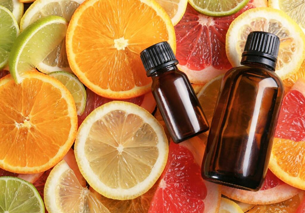 Two small amber bottles lying on a colorful background of various citrus fruit slices including oranges, lemons, limes, and grapefruits.