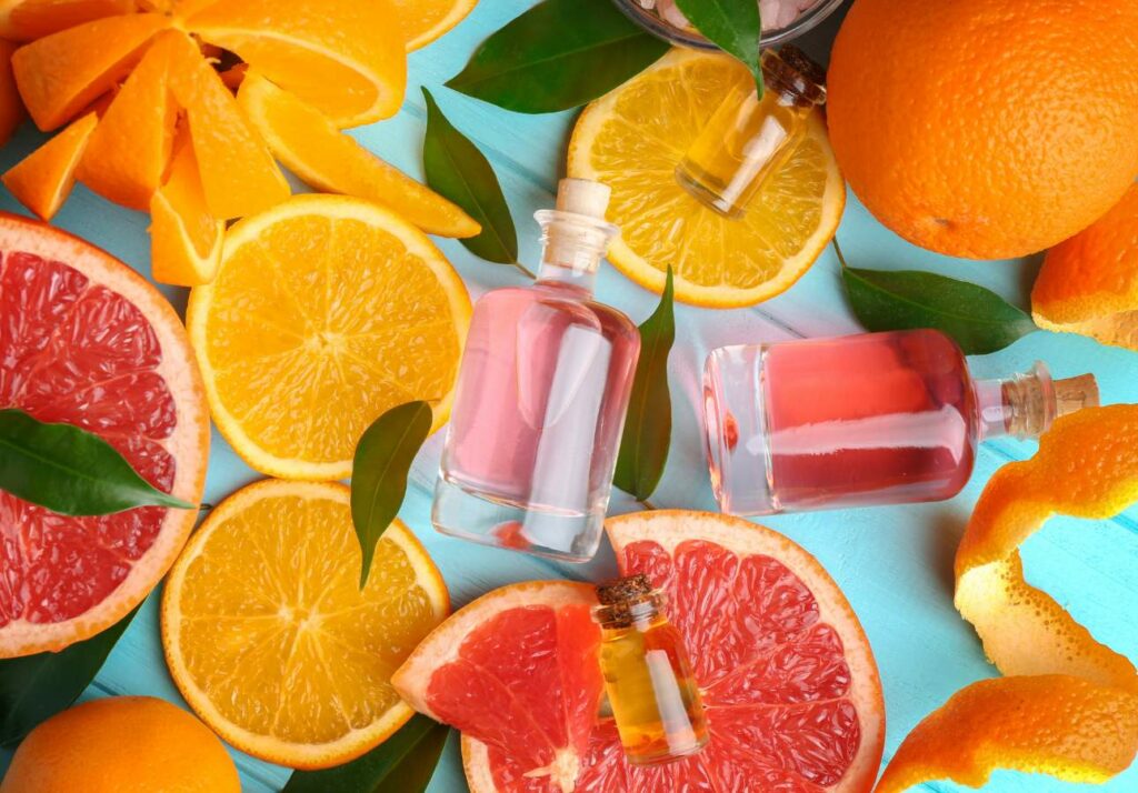 Glass bottles of essential oil surrounded by a variety of citrus fruits and leaves on a blue surface.