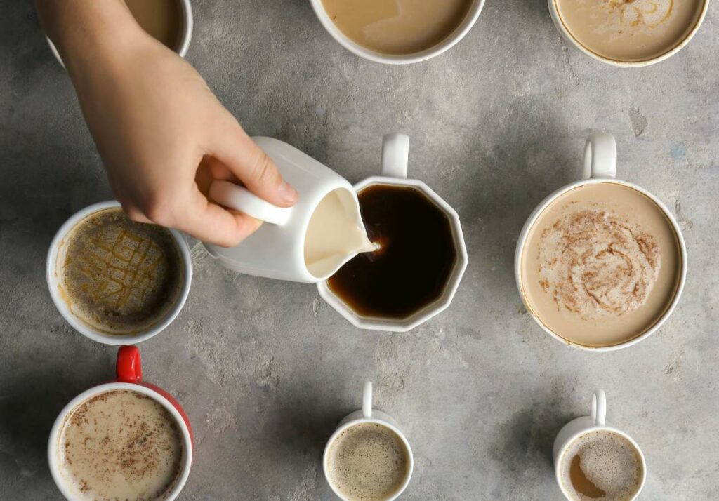 A person pouring coffee into cups, each containing different amounts of milk, top view on a gray surface.