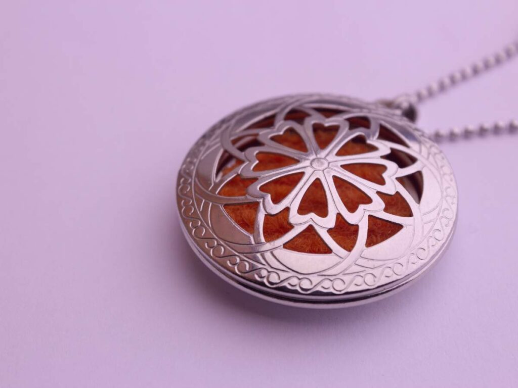 A close-up of a silver pendant with an intricate floral design, featuring an orange background, hanging from a beaded chain on a light purple surface.