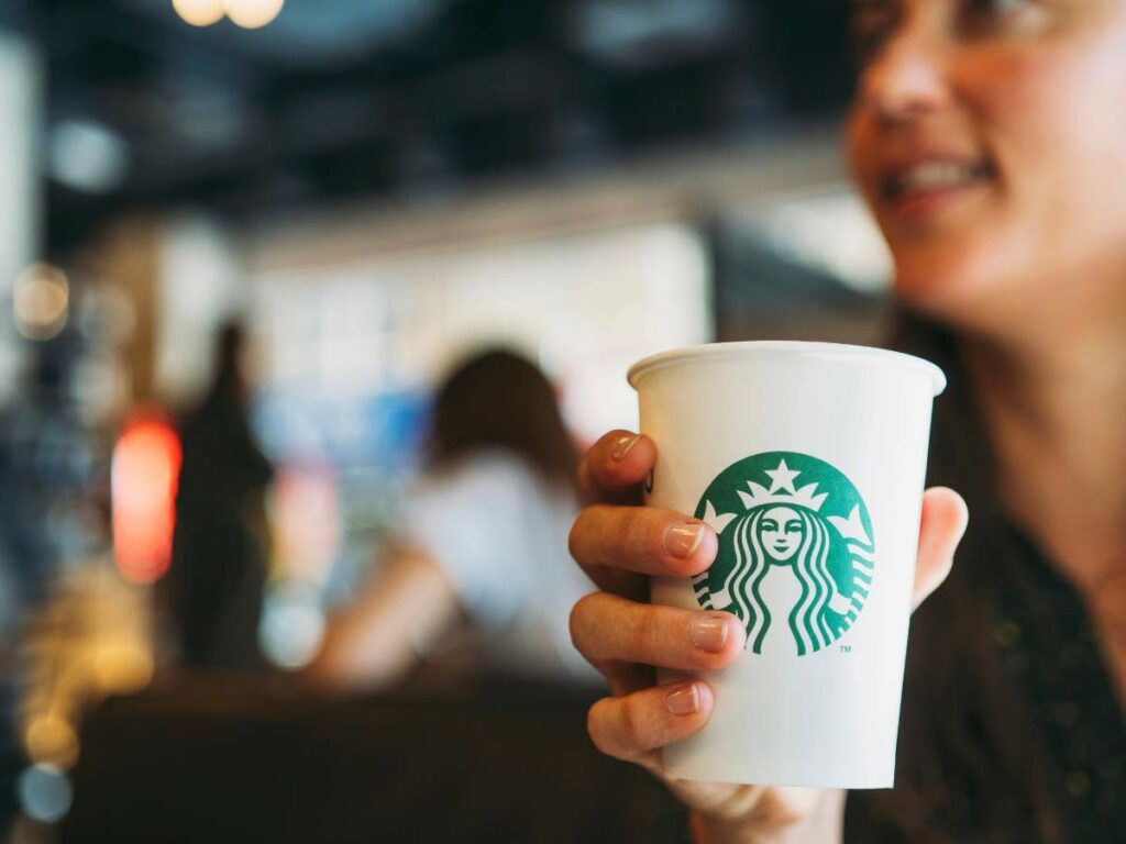 Person holds a white Starbucks cup inside a coffee shop.