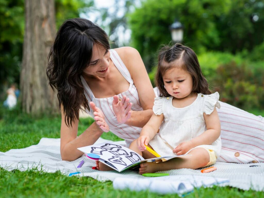 A woman and a child sit on a picnic blanket in a park.