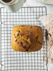 A freshly baked loaf of pumpkin bread cooling on a wire rack next to a lace cloth.