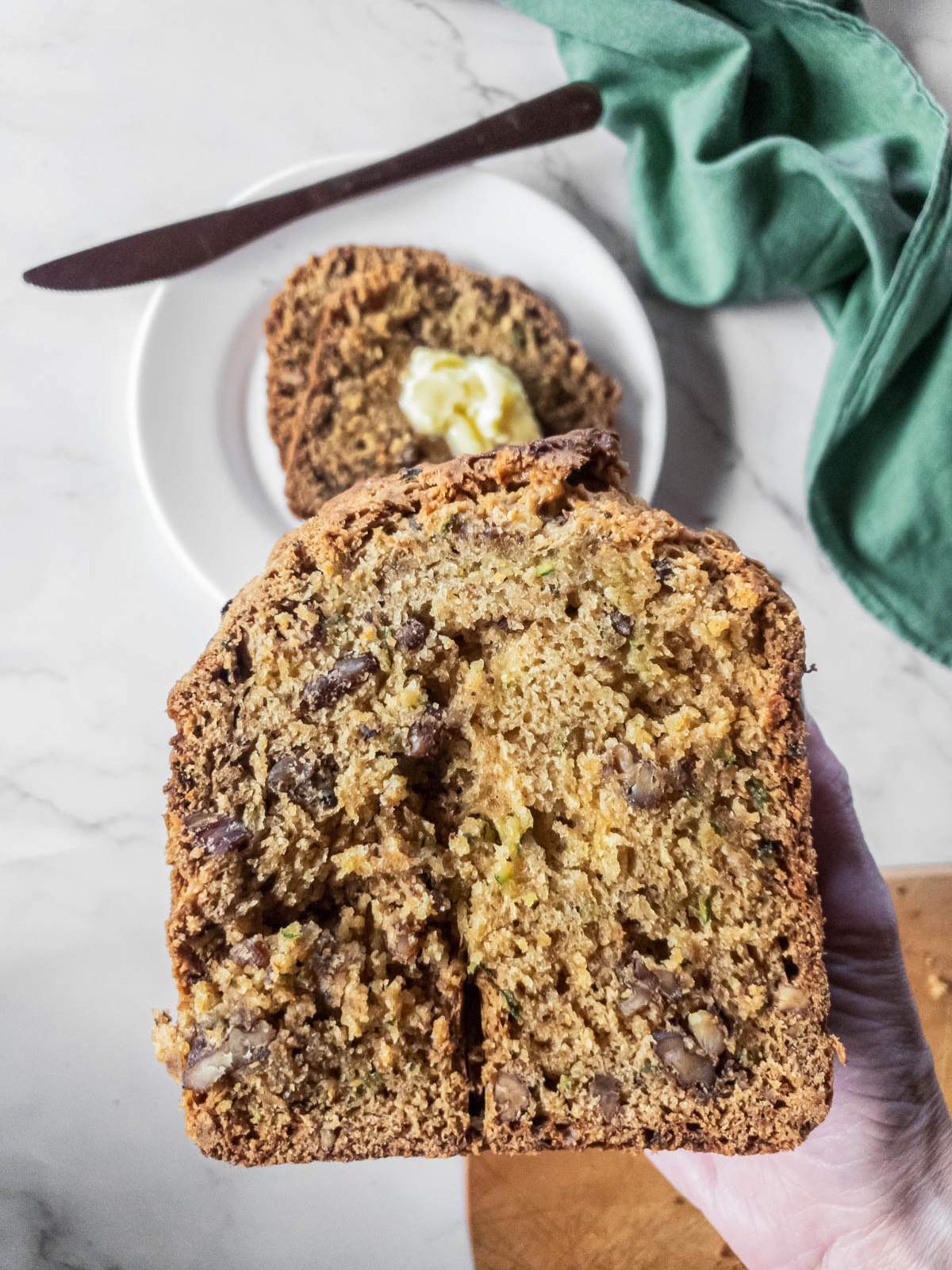 Close-up of a hand holding a slice of zucchini bread.