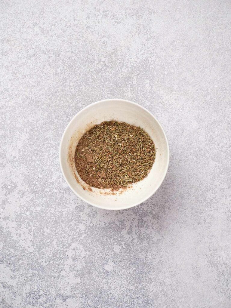 A white bowl containing a mixture of dried herbs and spices on a speckled gray surface.