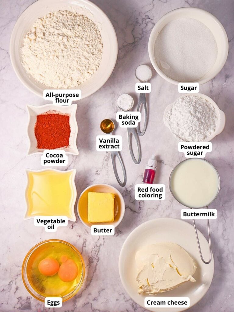 Ingredients for red velvet cake on a light colored surface, each labeled.