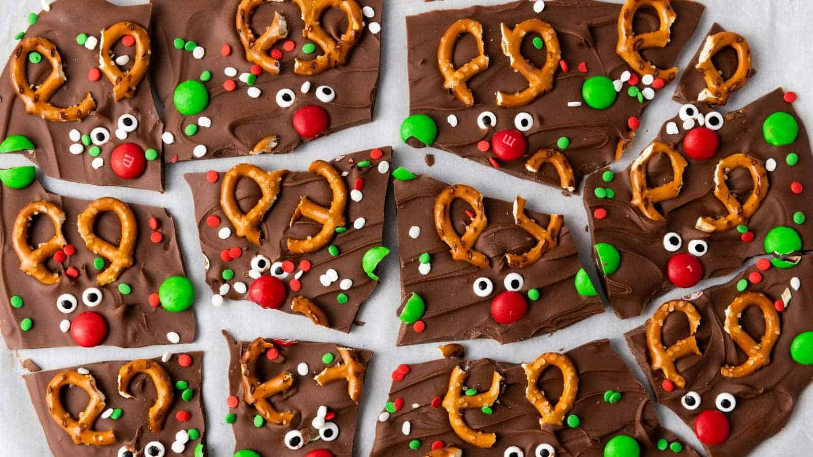 Chocolate bark pieces decorated with pretzel antlers, candy eyes, and red and green candies arranged like reindeer faces.
