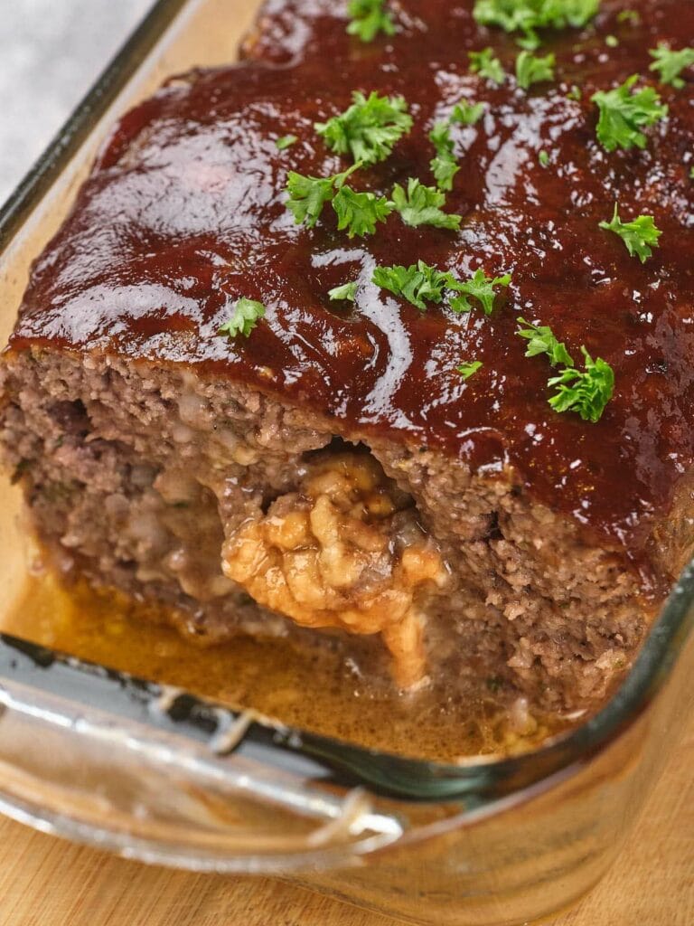 Close-up of stuffed meatloaf glazed with a sauce in a glass baking dish.