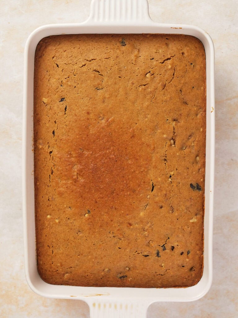 A rectangular baked dish with a golden-brown crust sits in a white ceramic baking dish.