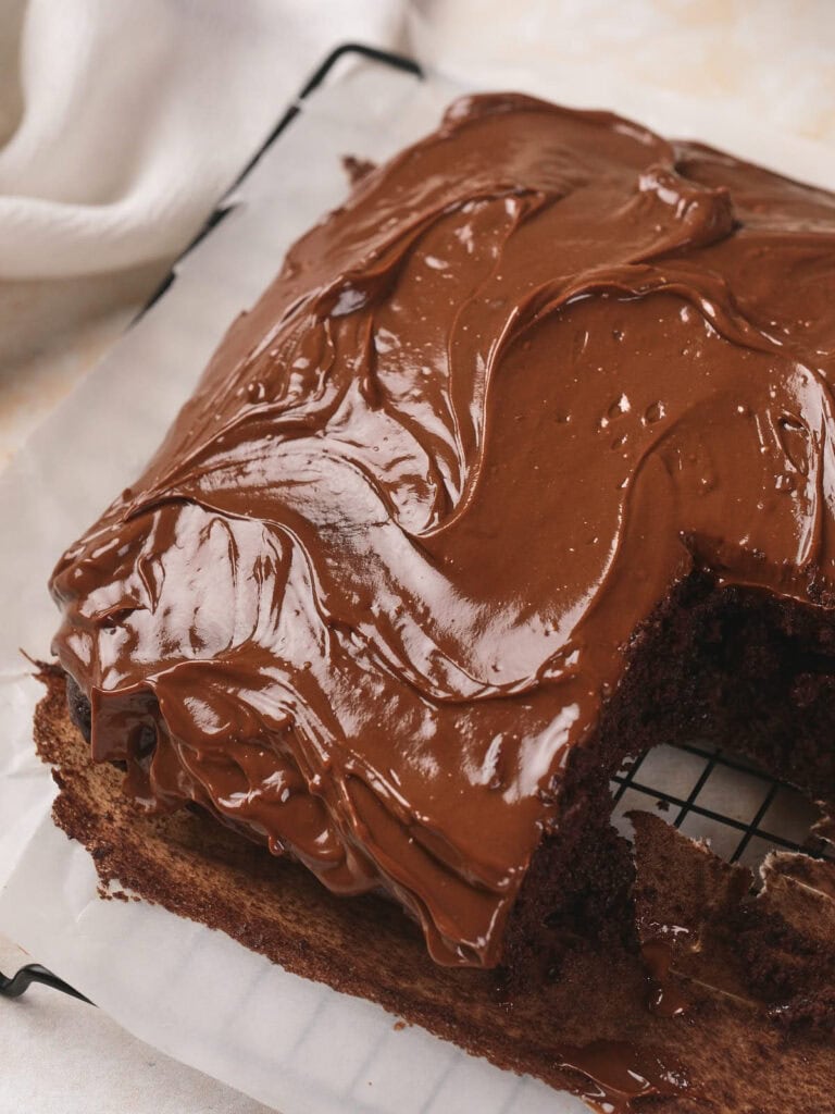 A rectangular chocolate fudge cake on a cooling rack, topped with glossy chocolate frosting.