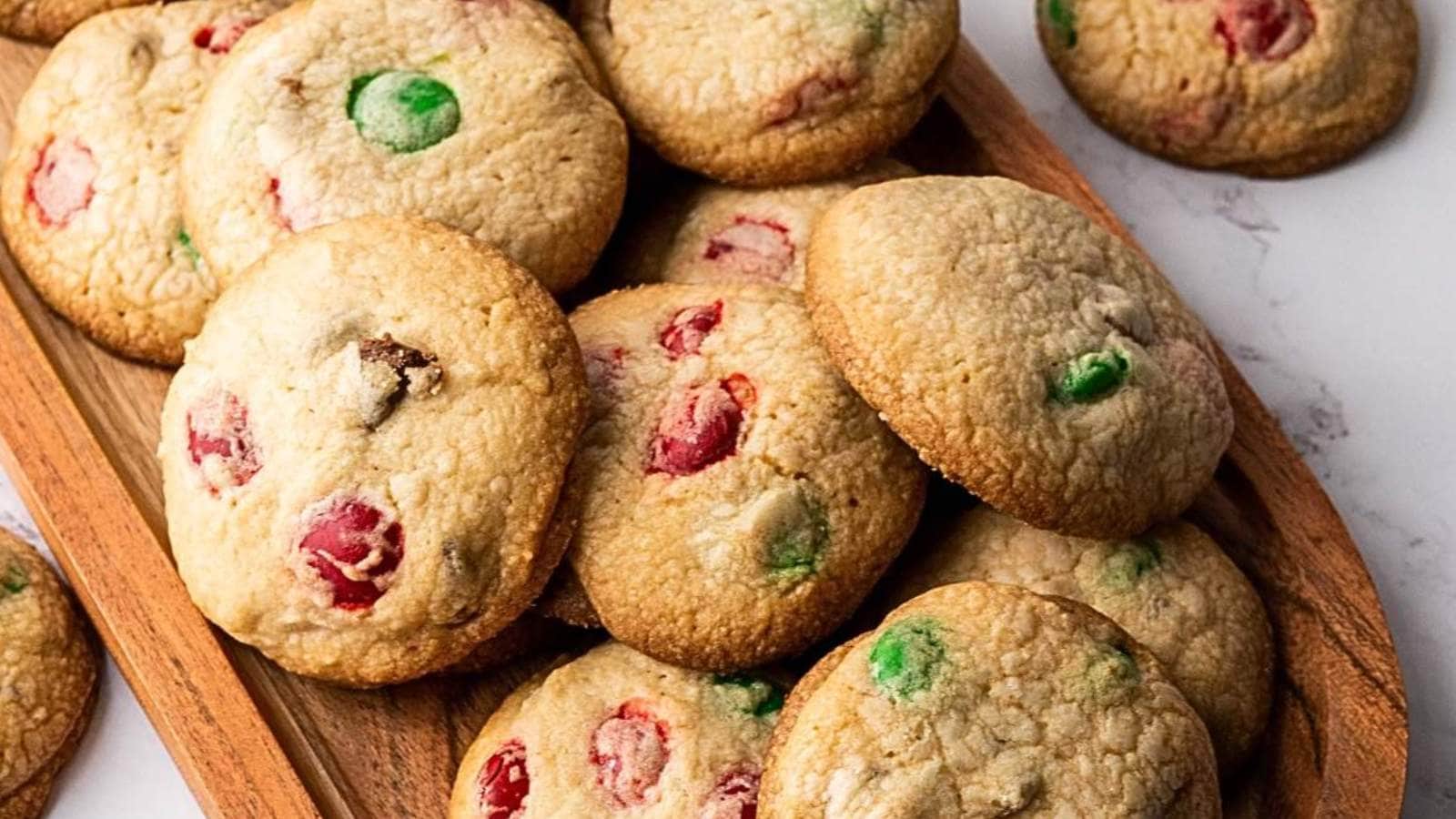 A wooden tray with assorted colorful candy cookies on a marble surface.