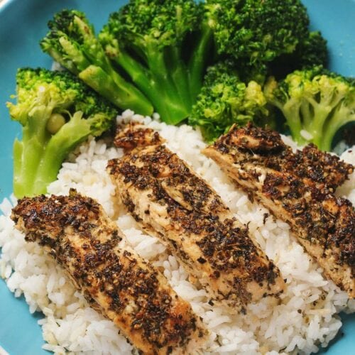 A blue plate with grilled herb-seasoned chicken strips on white rice, accompanied by steamed broccoli.