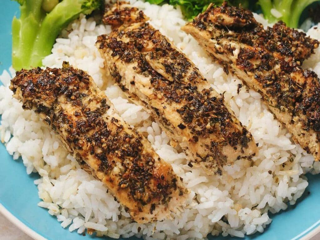 Grilled herb-seasoned chicken strips served on a bed of white rice, with a side of broccoli on a blue plate.