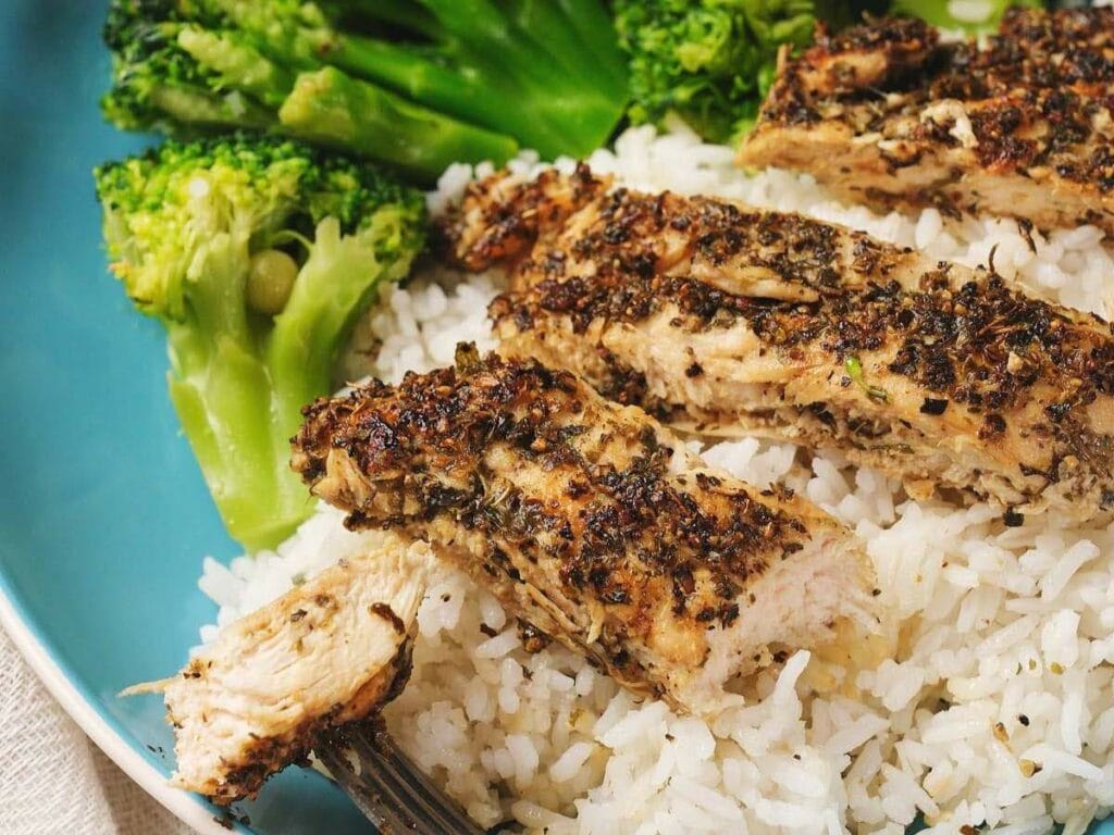 Grilled herb chicken on white rice with steamed broccoli on a blue plate.