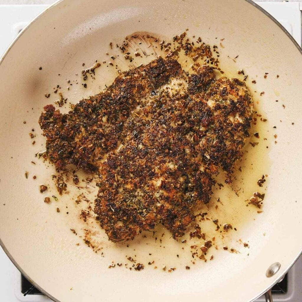 Chicken breast coated with herbs and spices, cooking in a pan.