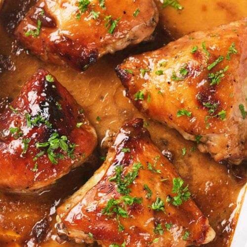 Four baked chicken thighs in apricot sauce, garnished with chopped parsley.