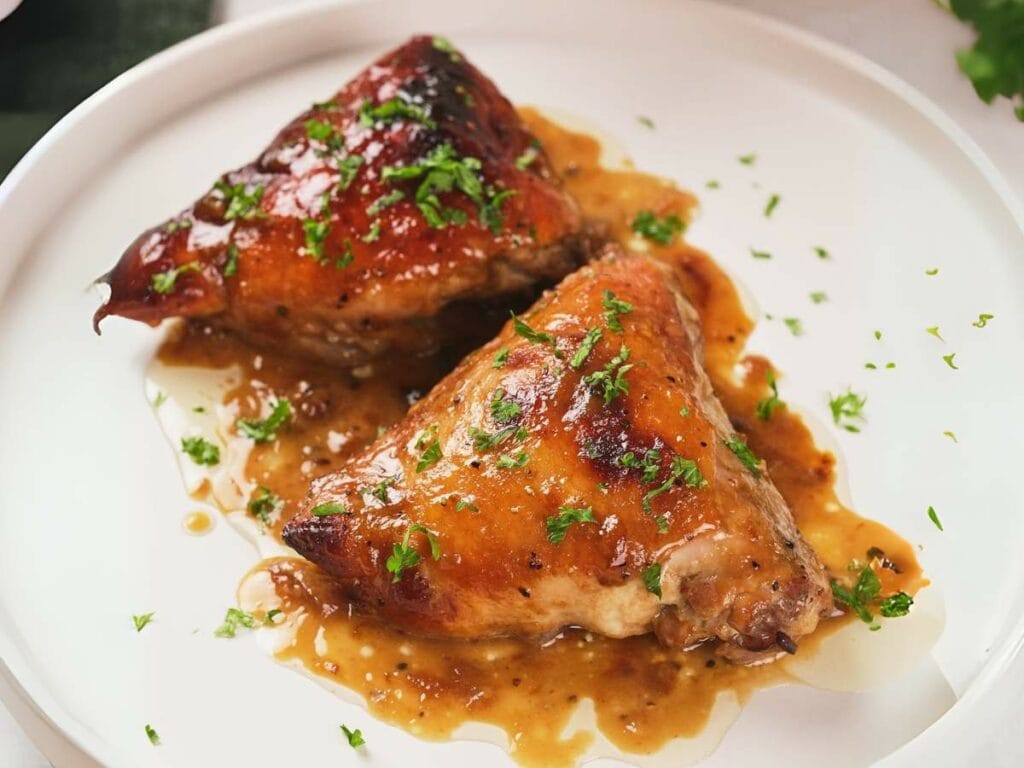 Two apricot chicken garnished with chopped herbs on a white plate, drizzled with a savory sauce.