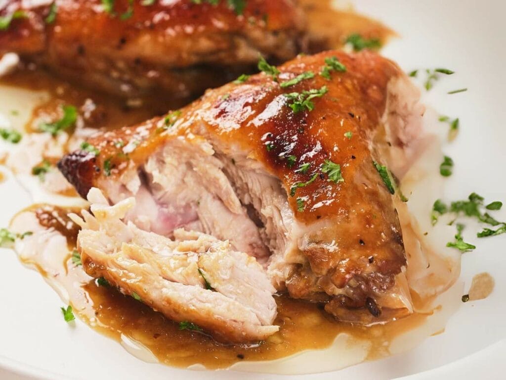 A close-up of chicken covered in apricot sauce, garnished with chopped parsley on a white plate.