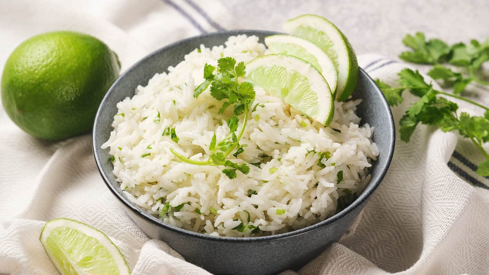 A blue bowl filled with chipotle rices. A whole lime is placed beside the bowl on a beige cloth.