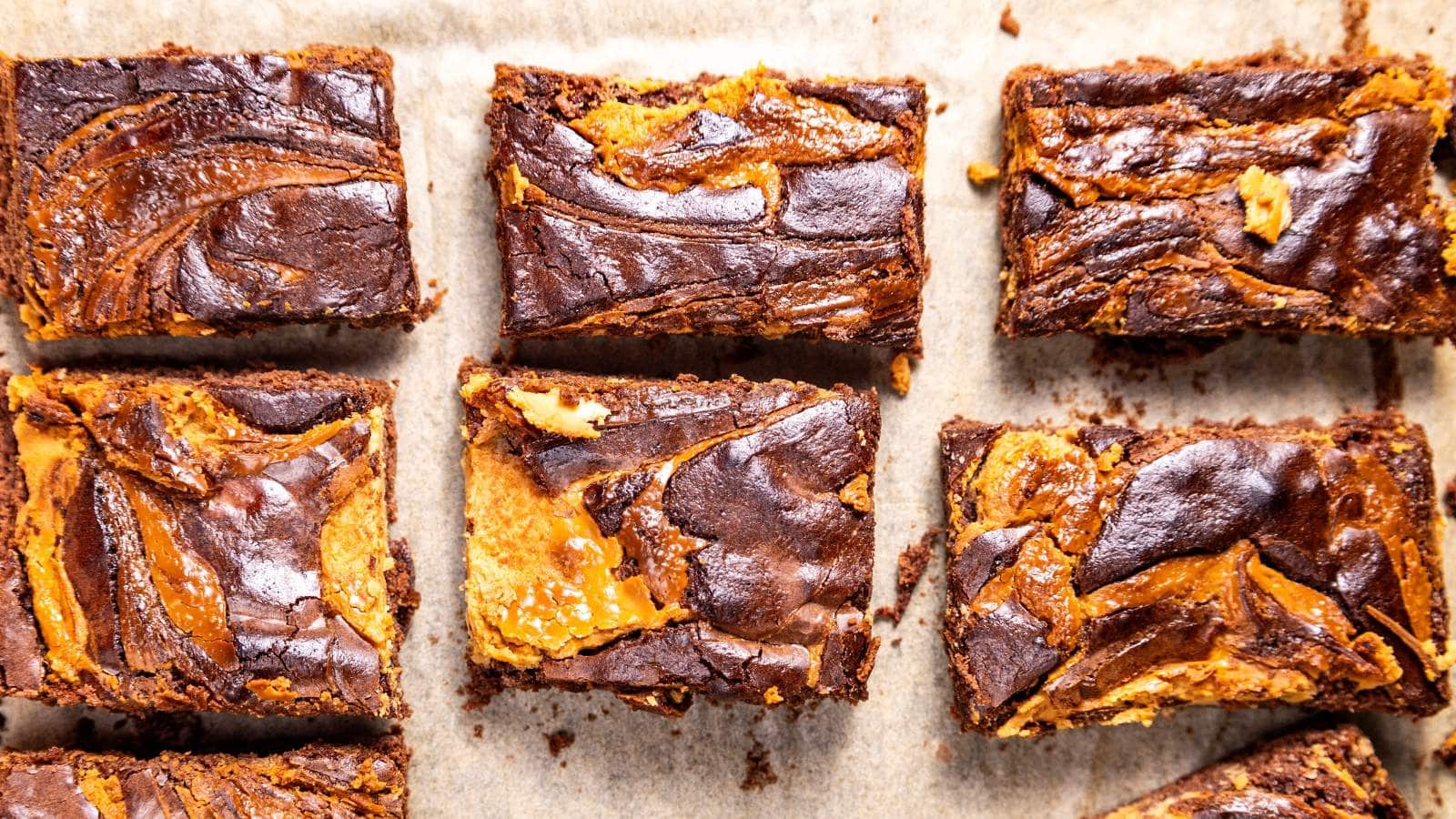 Six chocolate brownies with caramel swirls on parchment paper.