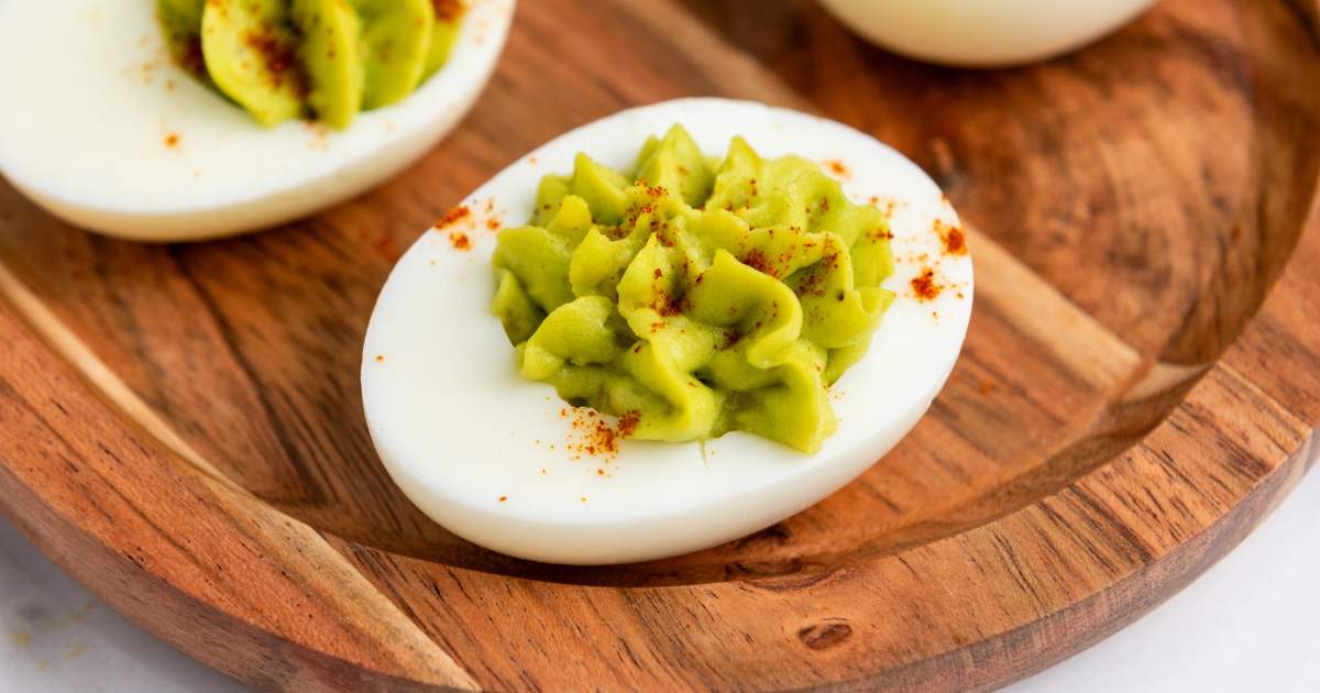 A deviled egg on a wooden plate, topped with green creamy filling and sprinkled with paprika.