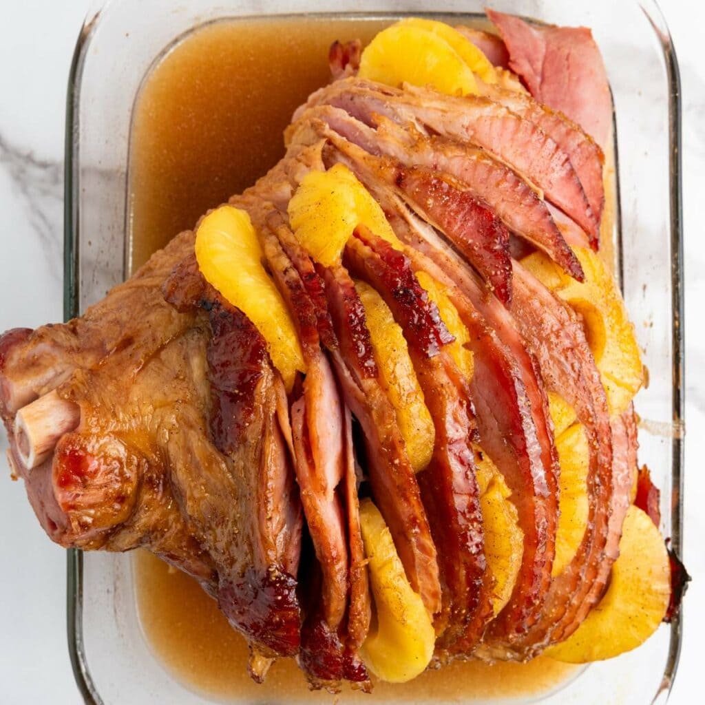 Glazed ham with pineapple slices in a glass baking dish.
