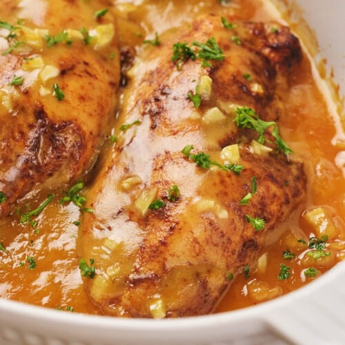 Honey mustard chicken with chopped parsley garnish, in a white dish.