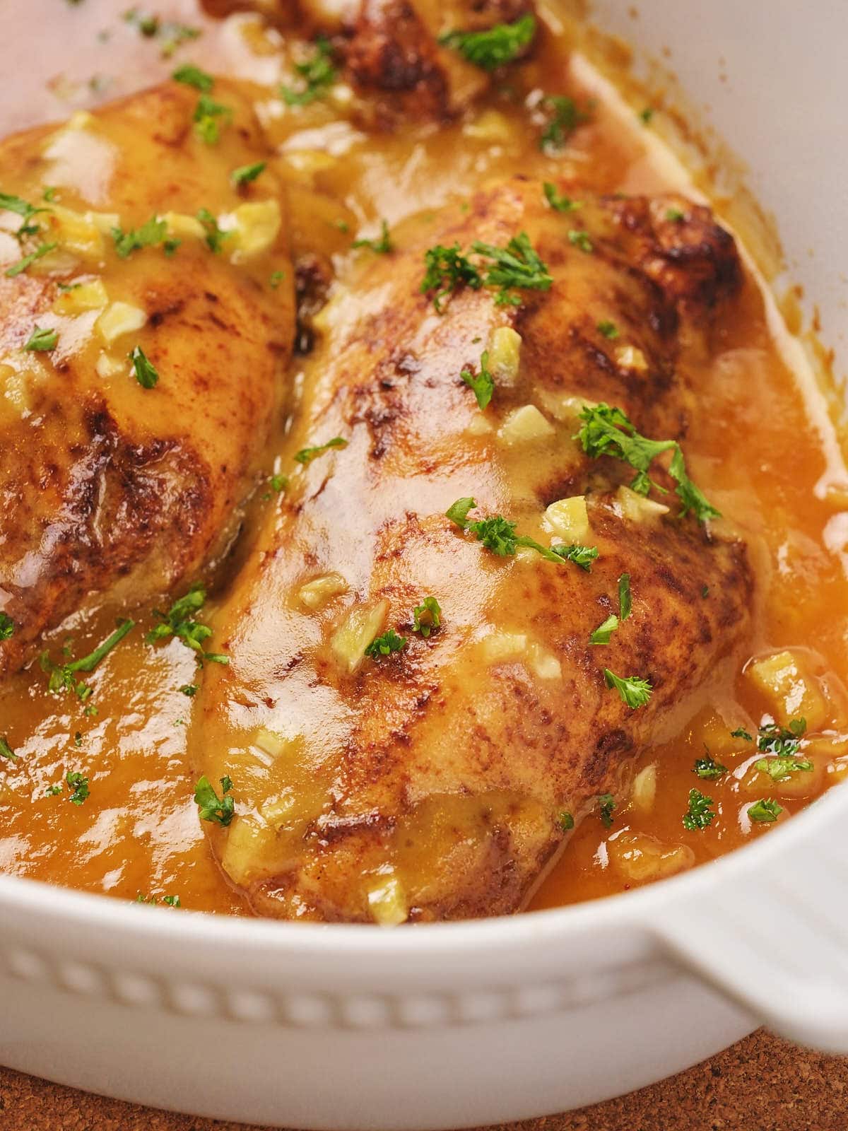 Honey mustard chicken with chopped parsley garnish, in a white dish.