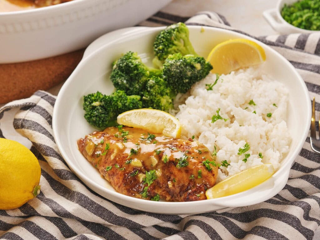 Plate of honey mustard chicken with lemon, rice, and broccoli, garnished with parsley.