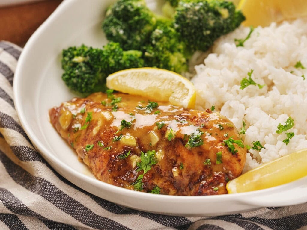 Plate with honey mustard chicken, served alongside broccoli, white rice, and lemon wedges.