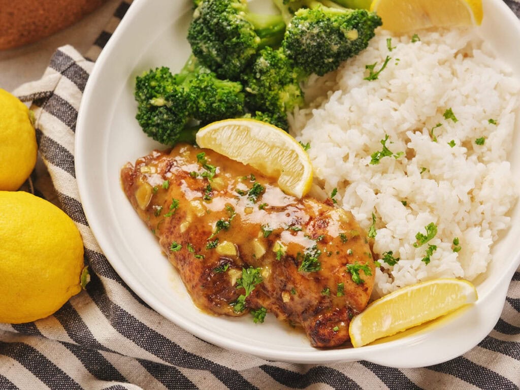 Plate with honey mustard chicken, served with white rice and broccoli on a striped cloth.