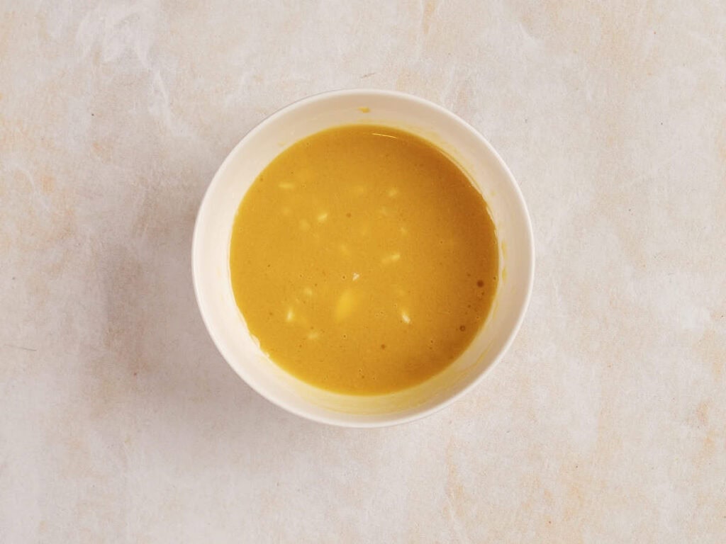 A bowl of yellow soup with small chunks, placed on a light-colored surface.
