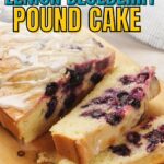 A sliced lemon blueberry pound cake with icing on a wooden board.
