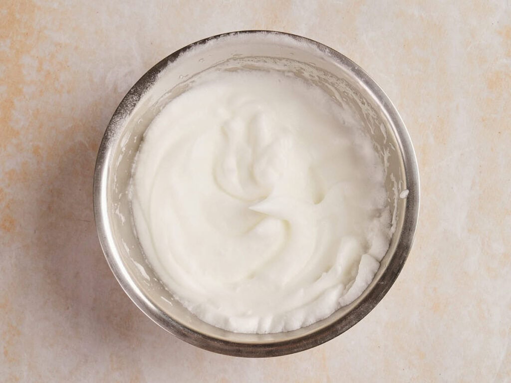 A metal bowl containing whipped egg whites on a light countertop.