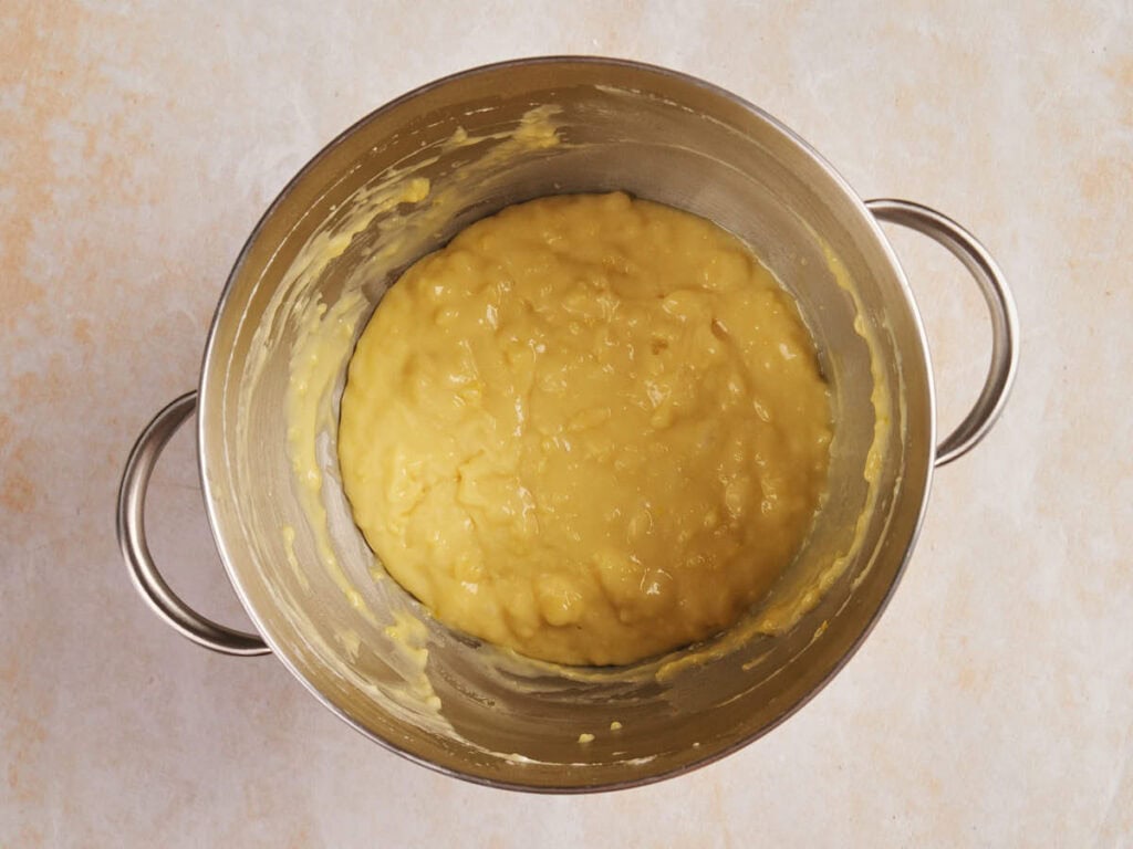A stainless steel pot containing thick, yellow mashed potatoes on a light-colored surface.