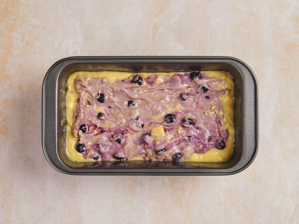 Batter with blueberries in a rectangular baking pan on a light countertop.
