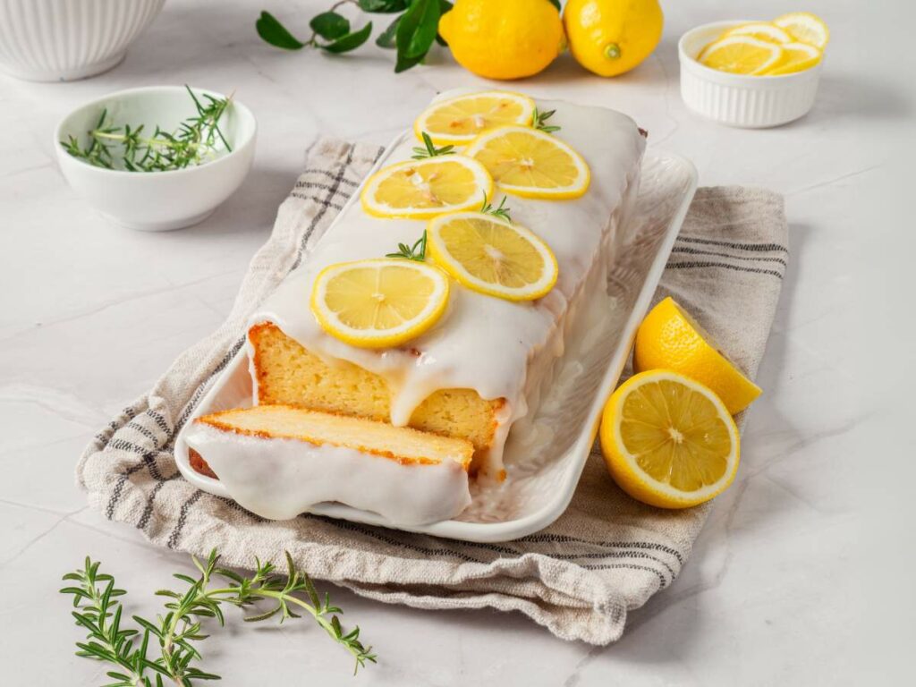 Lemon loaf cake on a platter with white glaze and lemon slices.