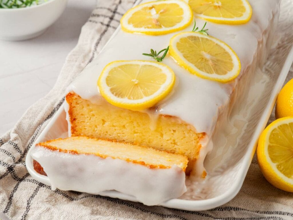 A glazed lemon cake topped with lemon slices on a rectangular white platter.