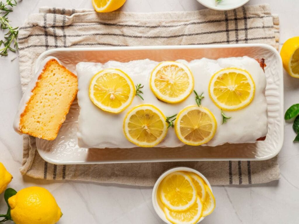 Lemon loaf cake with white glaze and lemon slices on top, placed on a rectangular tray.