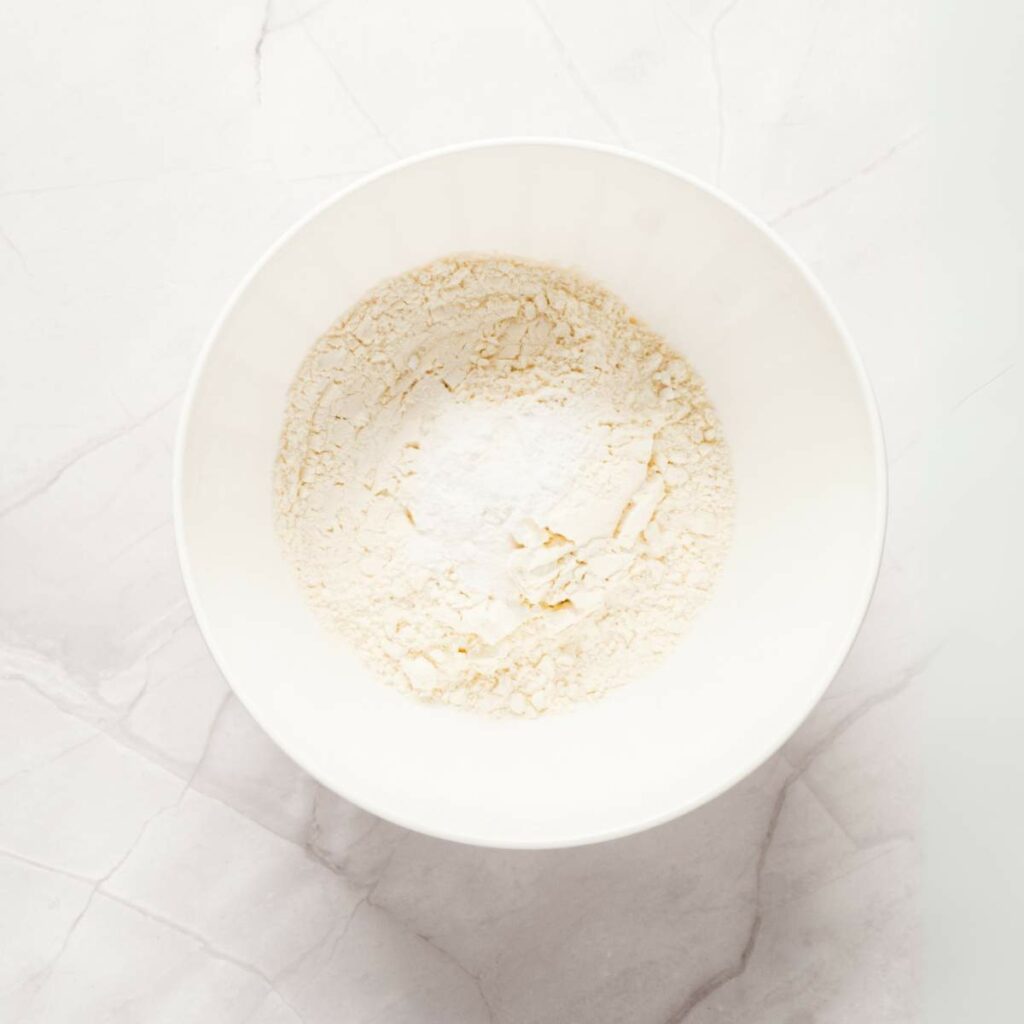 A white bowl containing flour on a light marble surface.